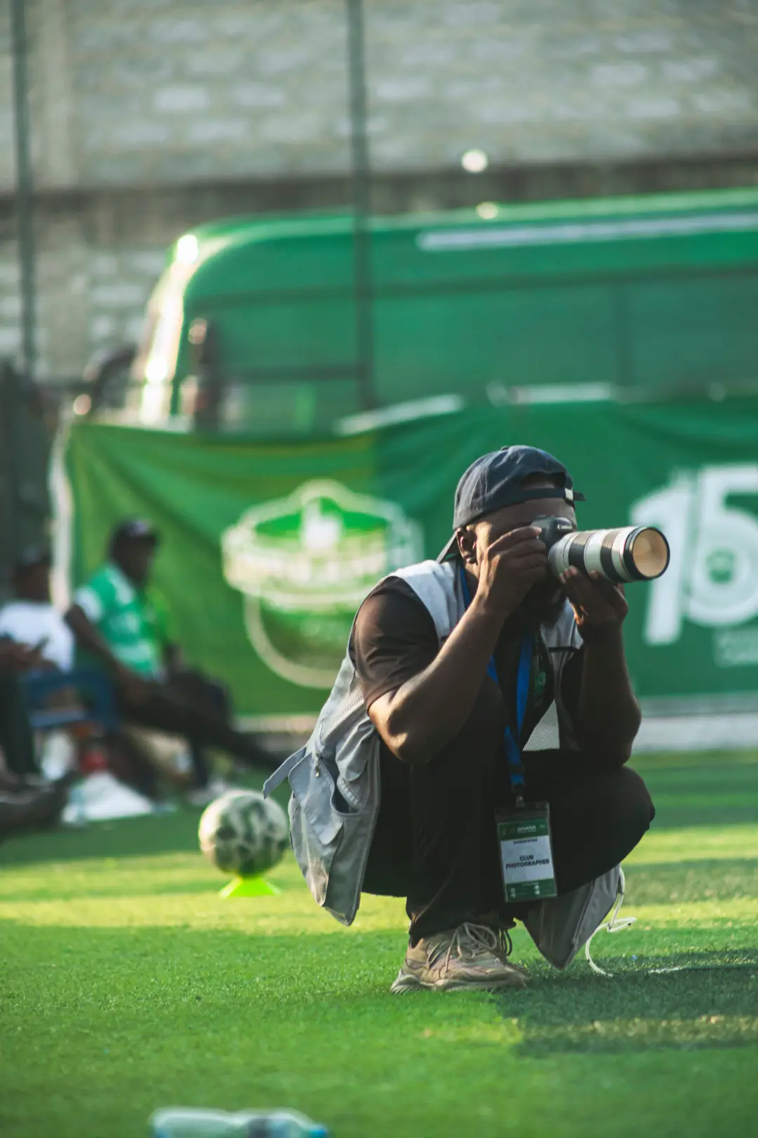 Photographer crouched on the sideline with a long lens