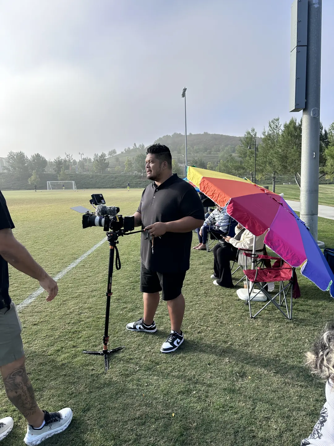 Videographer filming a game from the sideline with a camera on a tripod